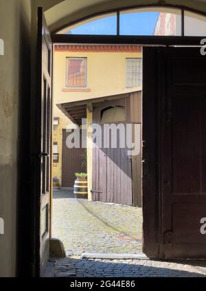 Halb geöffnetes Tor in einem alten Gebäude mit Blick in den Hof mit einem Holzfass Stockfoto