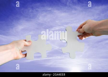 Menschliche Hände verbinden zwei Puzzleteile miteinander, Trockenbau, Himmelshintergrund Stockfoto