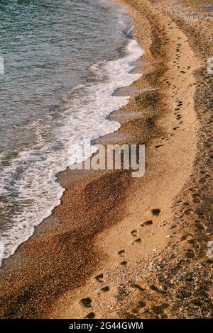 Kette von menschlichen Fußabdrücken erstreckt sich entlang des Strandes. Meeresbrandung Stockfoto