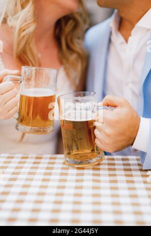 Ein Mann und eine Frau sitzen und umarmen sich Am Tisch und mit Bierkrügen Hände Stockfoto