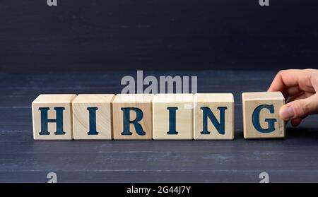 Weibliche Hand hält einen Balken mit der Aufschrift Hiring auf blauem Hintergrund. Rekrutierungskonzept Stockfoto