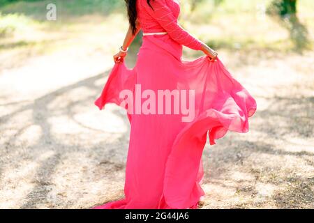 Eine Frau in einem stilvollen hot pink Kleid mit einem Langer Rock dreht sich auf einem trockenen Gras und hält Die Kanten des Rockes mit ihren Händen Stockfoto