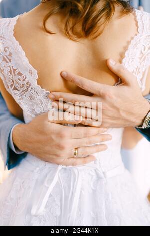 Nahaufnahme Hände des Bräutigams umarmen Braut an der Taille in einem weißen Spitzenkleid. Stockfoto