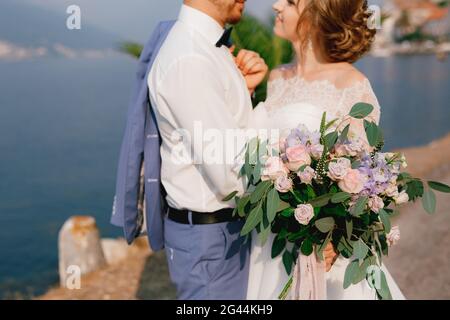 Braut und Bräutigam stehen umarmt am Pier, die Braut hält einen Blumenstrauß in der Hand, aus nächster Nähe Stockfoto