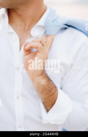 Ein Mann in einem weißen Hemd mit einem Ehering hält eine Jacke aus nächster Nähe über seine Schulter Stockfoto