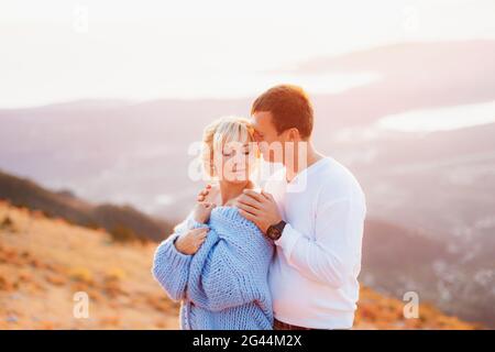 Der Mann umarmt die Frau in einem blauen Pullover an den Schultern Vor dem Hintergrund des Mount Lovcen Stockfoto