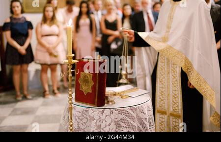 Hochzeitszeremonie in einer orthodoxen Kirche. Der Priester in einer weißen Soutane steht in der Kirche am Altar, Kerzen und bibel bei h Stockfoto