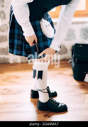 Vorbereitung auf eine schottische Hochzeit. Mann in hohen Socken, Sporran und Schuhen mit langen Schnürsenkeln befestigt ein kleines Schwert am Kilt Stockfoto