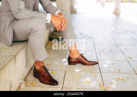 Ein Mann in einem grauen Anzug und braunen Lederschuhen Sitzt mit gefalteten Händen auf der Stufe Stockfoto