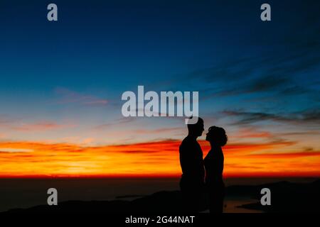 Silhouetten eines Paares, das die Hände vor dem Hintergrund des Sonnenuntergangs in den Bergen hält. Nahaufnahme Stockfoto