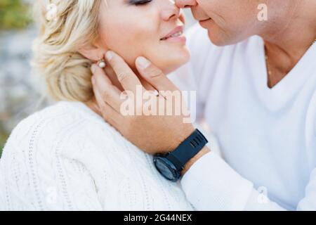 Mann in einem weißen Pullover und einer schwarzen Uhr küsst ein Frau in einem weißen Pullover und schönen Ohrringen Stockfoto