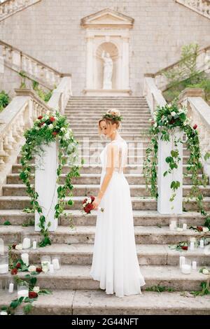 Sanfte Braut mit einem Hochzeitsstrauß in der Nähe der Säulen mit Blumen und Kerzen auf der alten Treppe des Tempels in P dekoriert Stockfoto