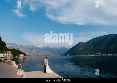 Das Brautpaar umarmt sich am Pier vor dem Hintergrund des Meeres und der grünen Berge. Perast Stadt, Montenegro Stockfoto