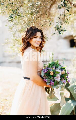 Schöne Braut in einem luxuriösen Pastellkleid niedlich lächelnd halten Ein Blumenstrauß in ihren Händen Stockfoto