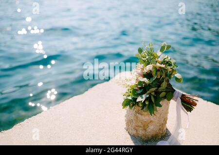 Brautstrauß von rosa protea, Ästen von Eukalyptusbäumen, rosa Rosen, Capsella und weißen Bändern am Seebrücke in der Nähe des Wate Stockfoto