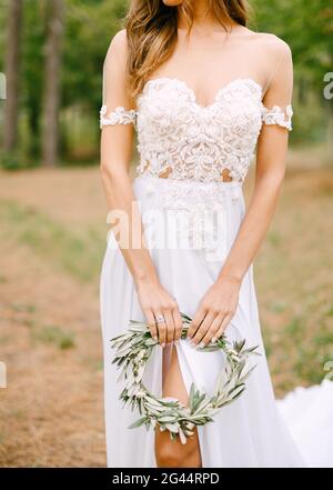 Stilvolle Braut in einem Spitzen-Kleid mit einem Ausschnitt Auf dem Bein einen Kranz aus Olivenzweigen haltend Stockfoto