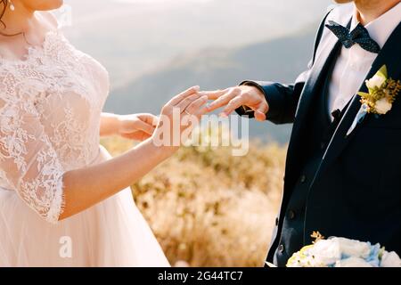 Braut in einem schönen Kleid setzt einen Ring auf die Finger des Bräutigams Stockfoto