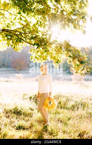 Frau, die einen Kranz aus gelben Blättern unter einem Baum hält Im Herbstwald Stockfoto