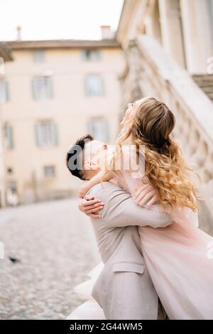 Bräutigam hält die Braut vor dem Hintergrund eines alten Gebäudes in Bergamo, Italien, in den Armen Stockfoto