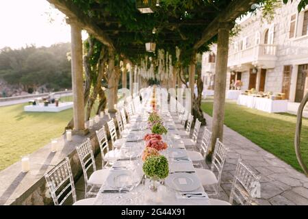 Hochzeitsessen Tischempfang. Ein sehr langer Tisch für Gäste mit weißer Tischdecke, Blumenarrangements, Glas-Kunststoff-Transpa Stockfoto