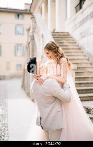 Bräutigam hält die Braut in den Armen nahe der Treppe eines alten Gebäudes in Bergamo, Italien. Nahaufnahme Stockfoto