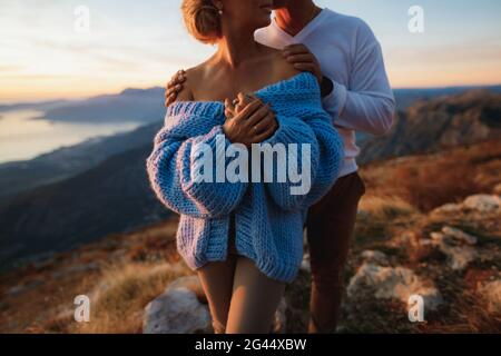 Der Mann umarmt eine Frau in einem blauen Pullover an den Schultern auf dem Hintergrund der Berge. Nahaufnahme Stockfoto