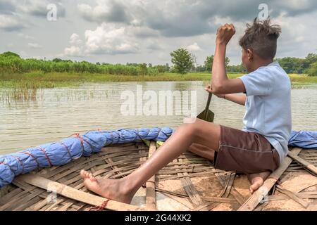 Junger Teenager, ein Dorfbewohner, der traditionelles Corakel rudert, um einen überfluteten Fluss in einem Vorort des Dorfes zu überqueren. Schöne indische Szene des ländlichen Lebensstils. Stockfoto