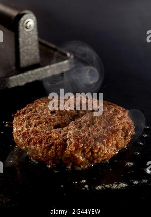 Dickes, saftiges Rindfleisch-Patty, das auf dem Grill mit waftng Dampf in einer vertikalen Ansicht mit hohem Winkel und Kopffunktion brutzelt Stockfoto