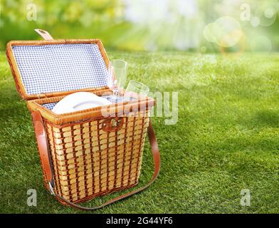 Sommer- und Frühlingshintergrund mit offenem Korbkorb mit Picknick-Accessoires, die an sonnigen Tagen auf einer grünen Wiese mit verschwommener Wirkung platziert werden Stockfoto