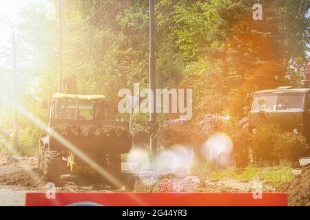 Ein Bulldozer baut eine Straße. Baumaschinen auf dem Hintergrund von grünen Bäumen. Sonneneinstrahlung. Das Konzept der Investition in den Bau von ro Stockfoto