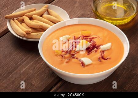 Salmorejo, spanische kalte Tomatensuppe, auf rustikalem Holzhintergrund mit picos und Olivenöl Stockfoto
