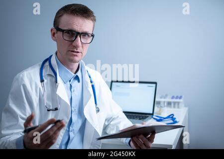 Der junge Arzt konsultiert den Patienten im Krankenhausbüro und hält medizinische Untersuchungen in den Händen. Allgemeinmediziner in weiß medi Stockfoto