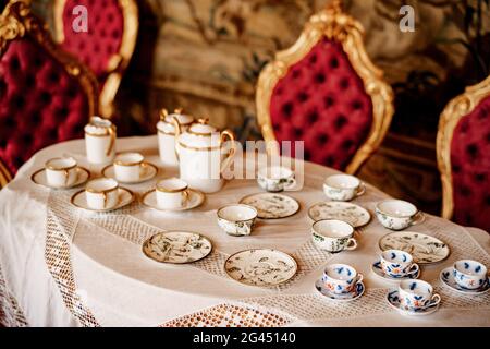 Ein Tee-Set mit einem blauen Muster und einem goldenen Set auf einem Tablett auf einem weißen Mantel mit Zierleiste vor dem Hintergrund einer roten Wand Witz Stockfoto