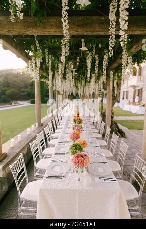 Hochzeitsessen Tischempfang. Ein sehr langer Tisch für Gäste mit weißer Tischdecke, Blumenarrangements, Glas-Kunststoff-Transpa Stockfoto