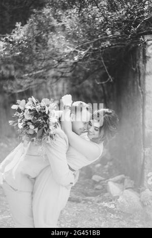 Schwarzweiß-Foto. Glücklich lächelnder Bräutigam umarmt Braut in einem schönen Kleid. Die Braut hält in ihren Händen einen großen Blumenstrauß Stockfoto