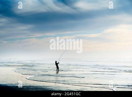 Silhouette eines Fischers, der am Strand unter blauem Himmel angeln soll Stockfoto
