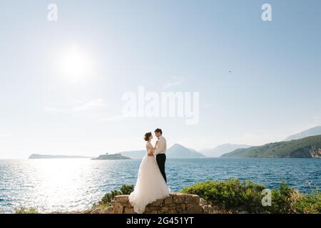 Braut und Bräutigam umarmen sich am Strand der Insel Mamula vor dem Hintergrund der Festung Arza Stockfoto