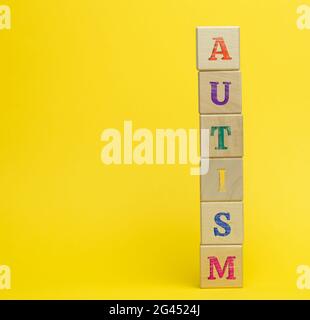 Holzwürfel mit der Aufschrift Autismus auf gelbem Hintergrund. Konzept der Unterstützung und Ermutigung für Kinder mit Entwicklungskindern Stockfoto