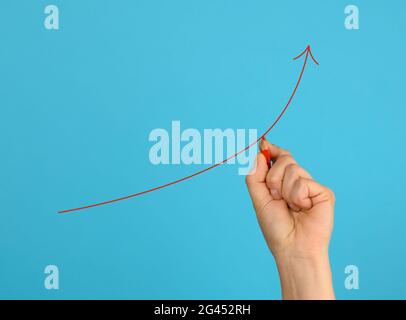 Weibliche Hand zeichnet einen roten Pfeil auf einem blauen Hintergrund. Das Konzept der Gewinnsteigerung Stockfoto