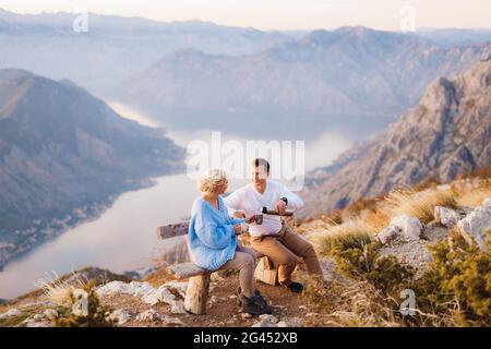 Das Paar sitzt auf einer Bank und trinkt Tee dagegen Hintergrund des Mount Lovcen und der Bucht von Kotor Stockfoto