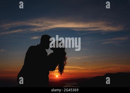 Silhouetten der Braut und Bräutigam, die umarmen und Küssen auf Mount Lovcen mit Blick auf die Bucht von Kotor at Sonnenuntergang Stockfoto