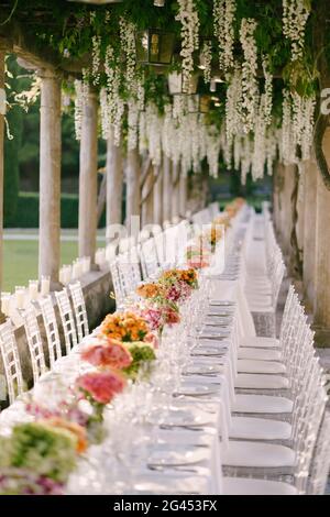 Hochzeitsessen Tischempfang. Ein sehr langer Tisch für Gäste mit weißer Tischdecke, Blumenarrangements, Glas-Kunststoff-Transpa Stockfoto