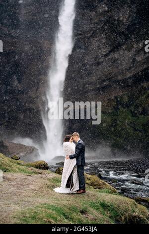 Destination Island Hochzeit, in der Nähe des Kvernufoss Wasserfalls. Das Brautpaar steht in der Nähe des Wasserfalls. Der Bräutigam umarmt die Braut. Stockfoto