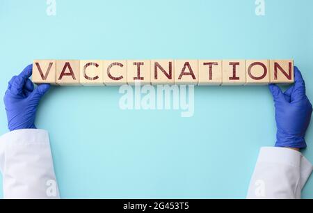 Arzthände in blauen Latexhandschuhen halten Würfel mit der Aufschrift Impfung auf blauem Hintergrund Stockfoto