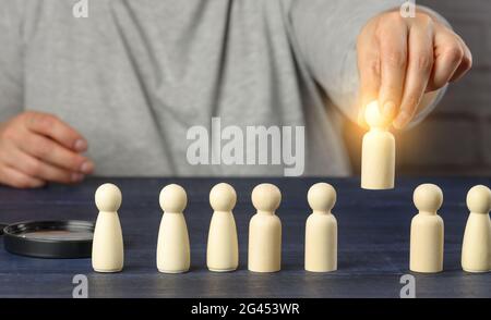 Eine weibliche Hand hält eine Holzfigur über der Menge. Das Konzept, Mitarbeiter, talentierte und einzigartige Mitarbeiter zu finden. Stockfoto