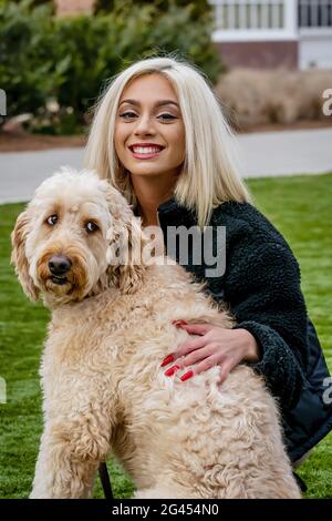 Ein junger reizender Blondes Modell posiert im Freien, während sie genießt Neuer Hund Stockfoto