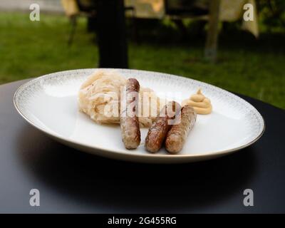 Nürnberger Grillwurst oder Nürnberger Rostbratwurst mit Sauerkraut oder saurem Kohl und Senf auf einem weißen Teller im Freien Stockfoto