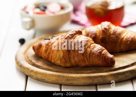 Leckere, wunderschöne Croissants auf Holzbrett. Traditionelles kontinentales Frühstück. Müsli mit Früchten und Honig auf dem Hintergrund. Stockfoto