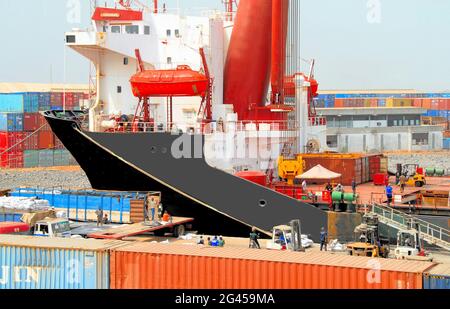 Ein im Hafen von Lomé, Togo, in Westafrika angedocktes Schiff entlädt Container, während die Container bereits hinten und vorne auf dem Foto gestapelt sind. Stockfoto