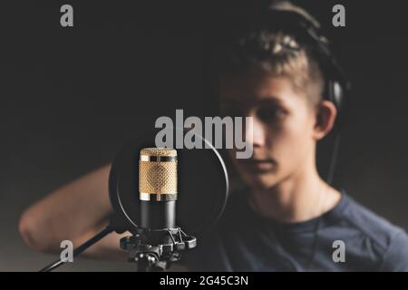 Stilvoller attraktiver Kerl mit Dreadlocks zeichnet im Studio einen Song auf. Ein junger Sänger in schwarzen Studio-Kopfhörern steht vor einem Mikrofon Stockfoto